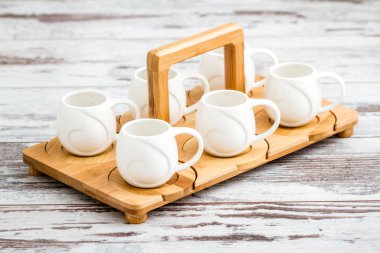 Porselen kahve fincanları beyaz ahşap bir masada bambu tepside dizilmişti..