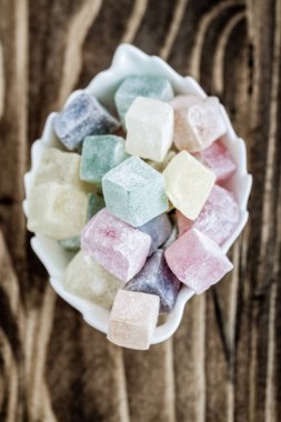 Koyu kahverengi ahşap arka planda sığ beyaz bir kâse içinde renkli pastel Türk lezzetleri.