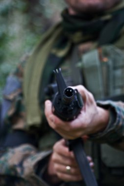 Yeşil ormanda, kamuflaj bezi giymiş, ateş etmek için hava tabancası kullanan bir asker..