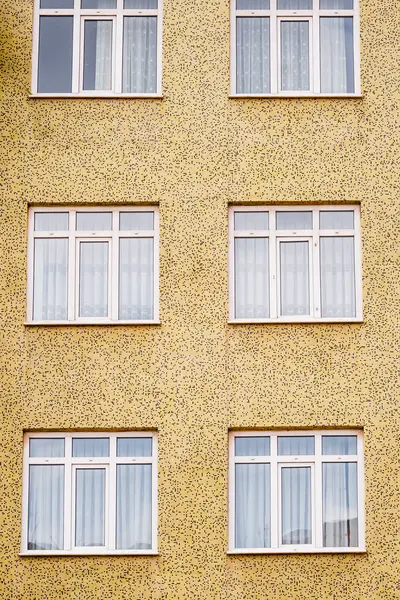 Sarı desenli bir binanın ön cephesinde iki sıra ve üç sıra halinde altı beyaz çerçeveli pencere var..