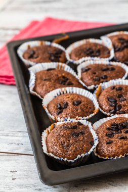Üstünde çikolata parçacıkları olan bir tepsi taze çikolatalı kek, kırmızı bir bez ve beyaz ahşap bir masa..