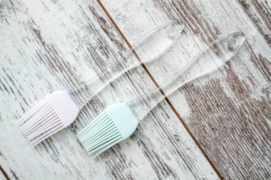 İki adet şeffaf saplı silikon fırça, biri pembe başlı ve diğeri açık mavi başlı, kırsal ahşap beyaz bir yüzeye yerleştirilmiş..