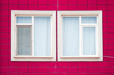 Pembe duvarları ve çift pencereli parlak renkli bina cephesi.