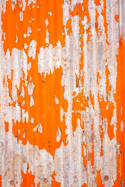 stock image Close up of a weathered corrugated metal surface with peeling orange paint, revealing rust and wear underneath.