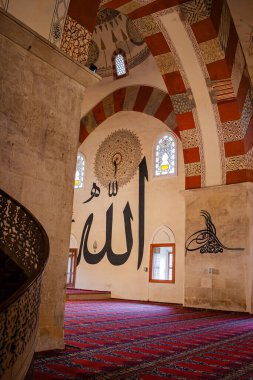 Türkiye 'nin Edirne kentindeki kırmızı desenli bir halıda, duvarlarında büyük Arapça yazı ve sütunları bulunan bir caminin içinde yürürken ve dua ederken görülüyor..
