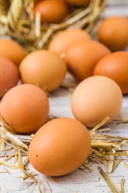 Taze kahverengi yumurtalar, biraz benekli, beyaz ahşap bir yüzeye saçılmış ve saman telleriyle çevrili, dokuma sepetinin ucunda.