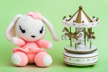 Amigurumi tavşan oyuncağı ve atlıkarınca canlı yeşil arka planda sergilenir.