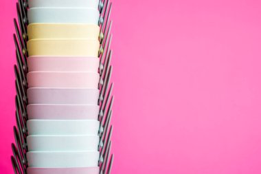 Renkli plastik bardaklar yığını, pembe bir arkaplana karşı pastel gökkuşağı renklerinde dizilmiş..