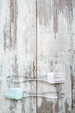 İki adet şeffaf kulplu silikon fırça, biri pembe başlı, diğeri açık mavi başlı, kırsal ahşap beyaz bir yüzeye yerleştiriliyor ve uzayı kopyalıyor.