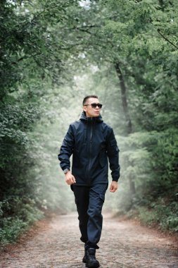 Siyah elbiseli vahşi bir adam sisli ormanda sokakta yürüyor.