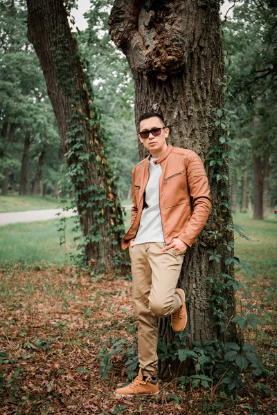 一个年轻英俊的男人站在秋天公园的一棵树下 — 图库照片