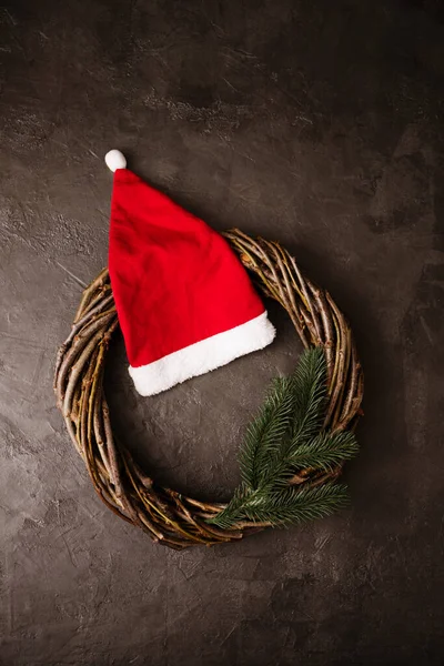 花环灰色背景上的树枝和红帽子做成的花环圣诞节的概念 — 图库照片