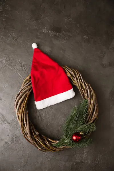 灰色の背景には 枝の花輪とサンタクロースの赤い帽子 クリスマスのコンセプト — ストック写真
