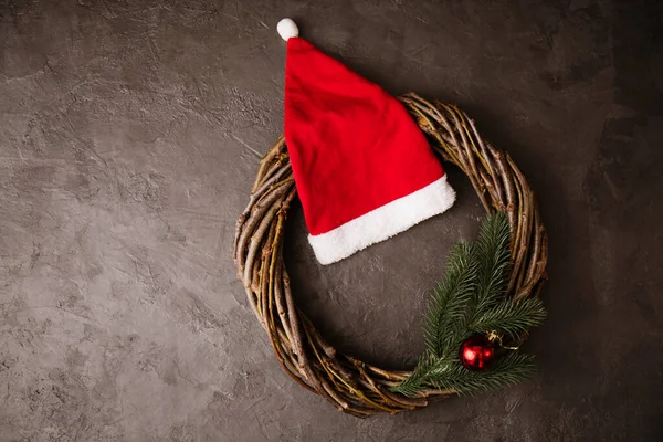 Ein Kranz Aus Zweigen Und Ein Roter Weihnachtsmannhut Auf Grauem — Stockfoto