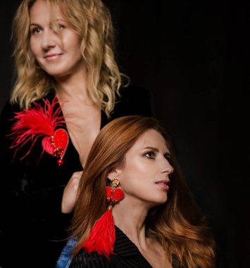 Kırmızı aksesuarlı iki genç kadın, bir broş ve bir küpe.