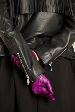 Siyah deri ceketli ve kısa mor eldivenli bir kadın.
