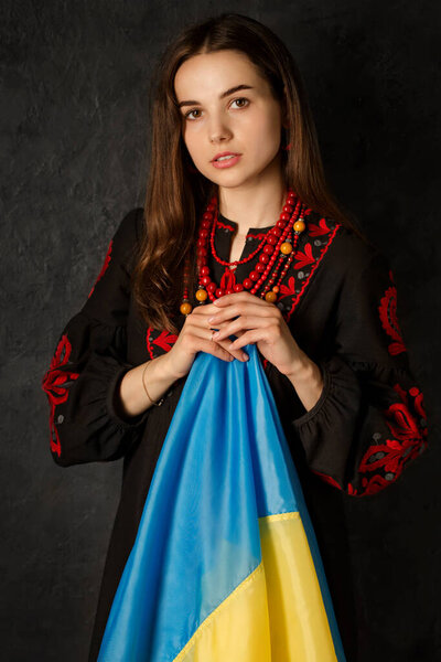 A beautiful Ukrainian woman in a national Ukrainian dress with a blue and yellow flag of Ukraine