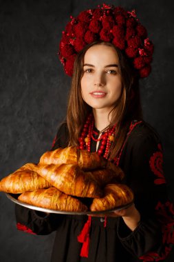 Ulusal elbiseli Ukraynalı kadın elinde pembe kruvasanlarla dolu bir tepsi tutuyor.