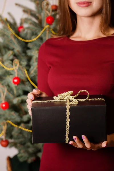 クリスマスツリーの近くに立っている若い女性がギフトボックスを持っています — ストック写真