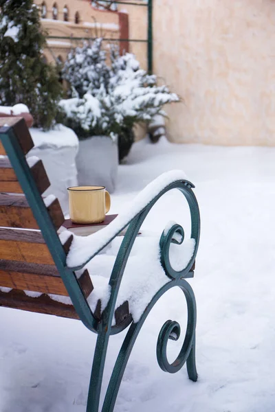 A snowy winter bench with books and a big cup of hot cocoa