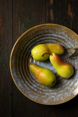 Koyu bir arka planda seramik kaselerde olgun sulu armutlar.