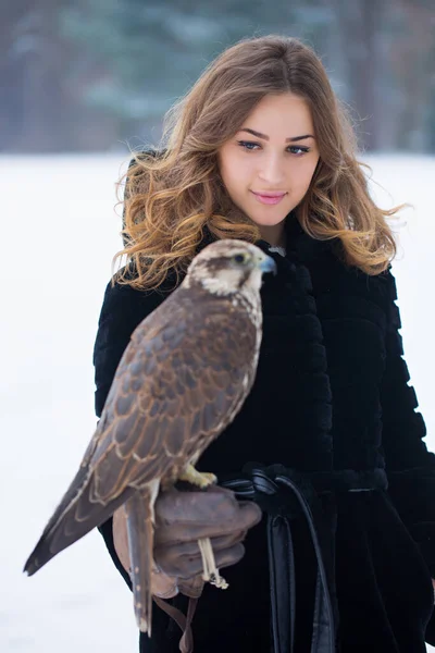 黒い毛皮のコートの女の子は冬に彼女の手に鷹を持っています — ストック写真