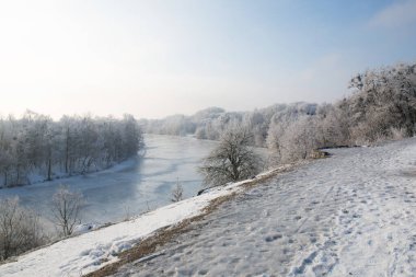 Güneşli bir kış sabahı, dağın eteğinde donmuş bir nehir.