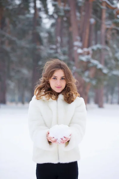 冬の雪の中で遊ぶ白い毛皮のコートの若い女性の肖像画 — ストック写真
