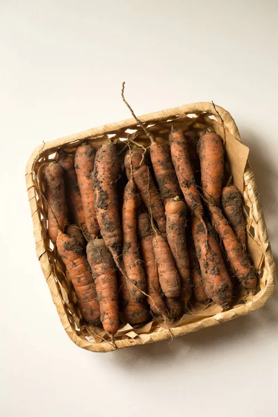 Fresh unwashed carrots in a square basket on a white background