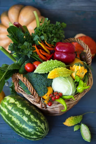 A large basket of various vegetables and fruits on a wooden background
