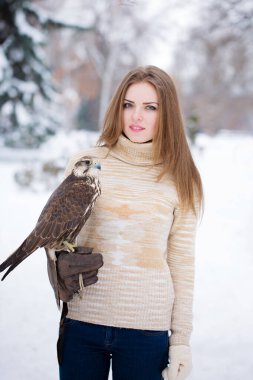 Siyah paltolu bir kız kışın elinde bir şahin tutuyor.