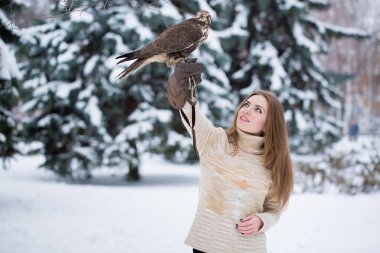 Siyah paltolu bir kız kışın elinde bir şahin tutuyor.