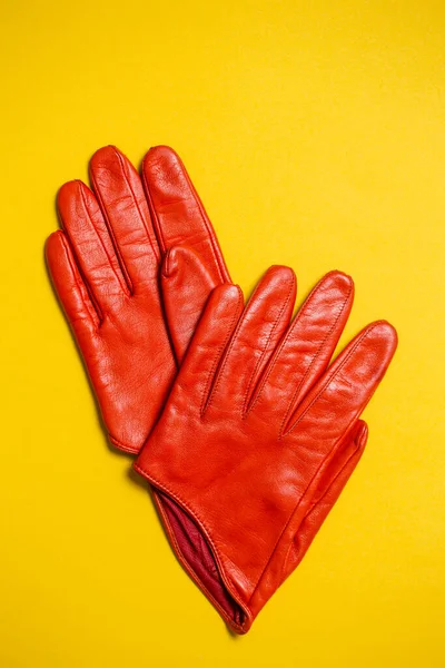 Short women's gloves made of orange leather on a yellow background