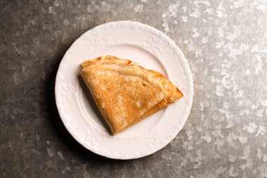 Metalik kaba bir zeminde beyaz bir tabakta kızarmış ince krep.