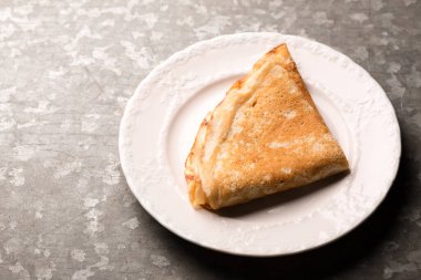 Metalik kaba bir zeminde beyaz bir tabakta kızarmış ince krep.