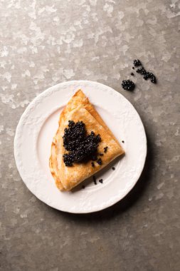 Lezzetli ince krep, metalik arka planda bir tabakta siyah havyar.