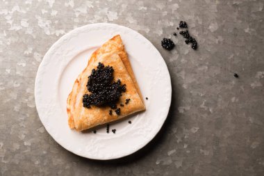 Lezzetli ince krep, metalik arka planda bir tabakta siyah havyar.