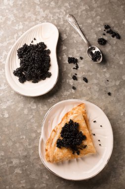 Lezzetli ince krep, metalik arka planda bir tabakta siyah havyar.