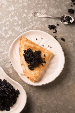 Lezzetli ince krep, metalik arka planda bir tabakta siyah havyar.