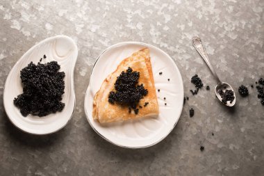 Lezzetli ince krep, metalik arka planda bir tabakta siyah havyar.