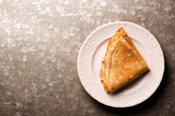 Metalik kaba bir zeminde beyaz bir tabakta kızarmış ince krep.