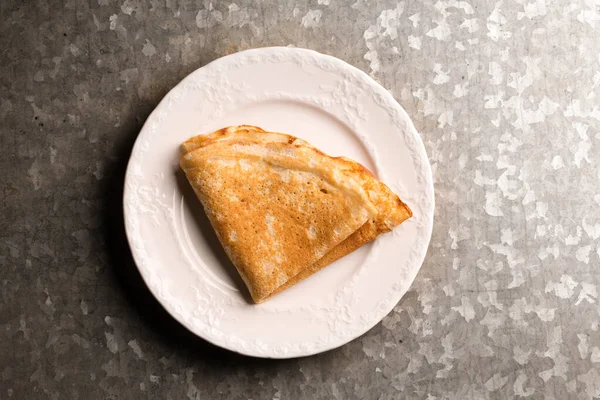 Metalik kaba bir zeminde beyaz bir tabakta kızarmış ince krep.