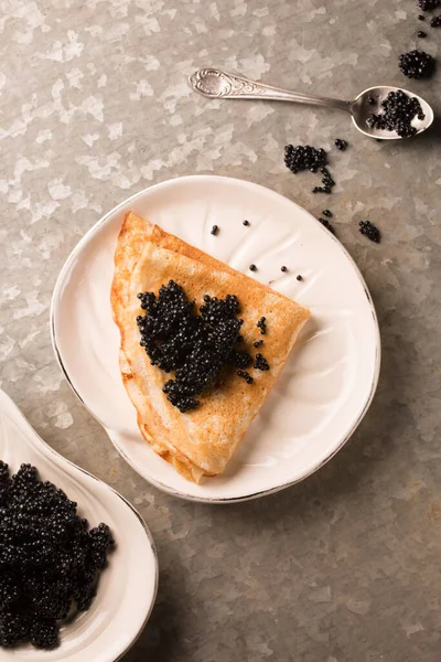 Lezzetli ince krep, metalik arka planda bir tabakta siyah havyar.