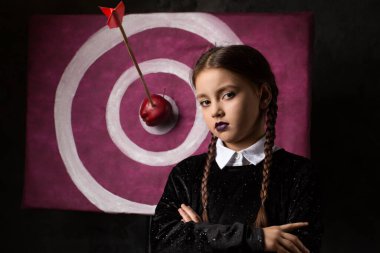 A gloomy girl with pigtails near a target with an arrow and an apple in a gothic style on a dark background