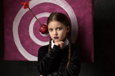 A gloomy girl with pigtails near a target with an arrow and an apple in a gothic style on a dark background