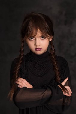 Portrait of a sullen girl with pigtails, hands folded sternly on a dark background