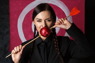 A beautiful woman bites an apple hit by an arrow against the background of  target a Viva Magenta color of 2023