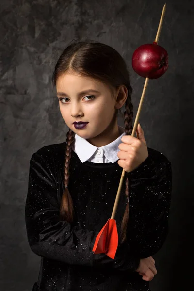 一个有着辫子的阴郁的女孩拿着一支箭 瞄准着一个深色背景的苹果 — 图库照片