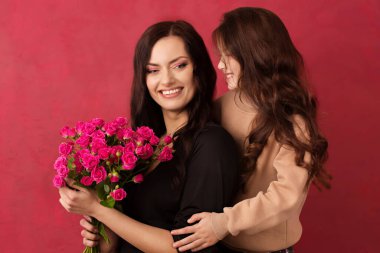 The girl greets her mother with a beautiful bouquet of pink roses on a pink background. Color of background Viva Magenta 18-1750, in 2023