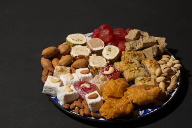 A large plate of various oriental sweets and nuts on a dark background